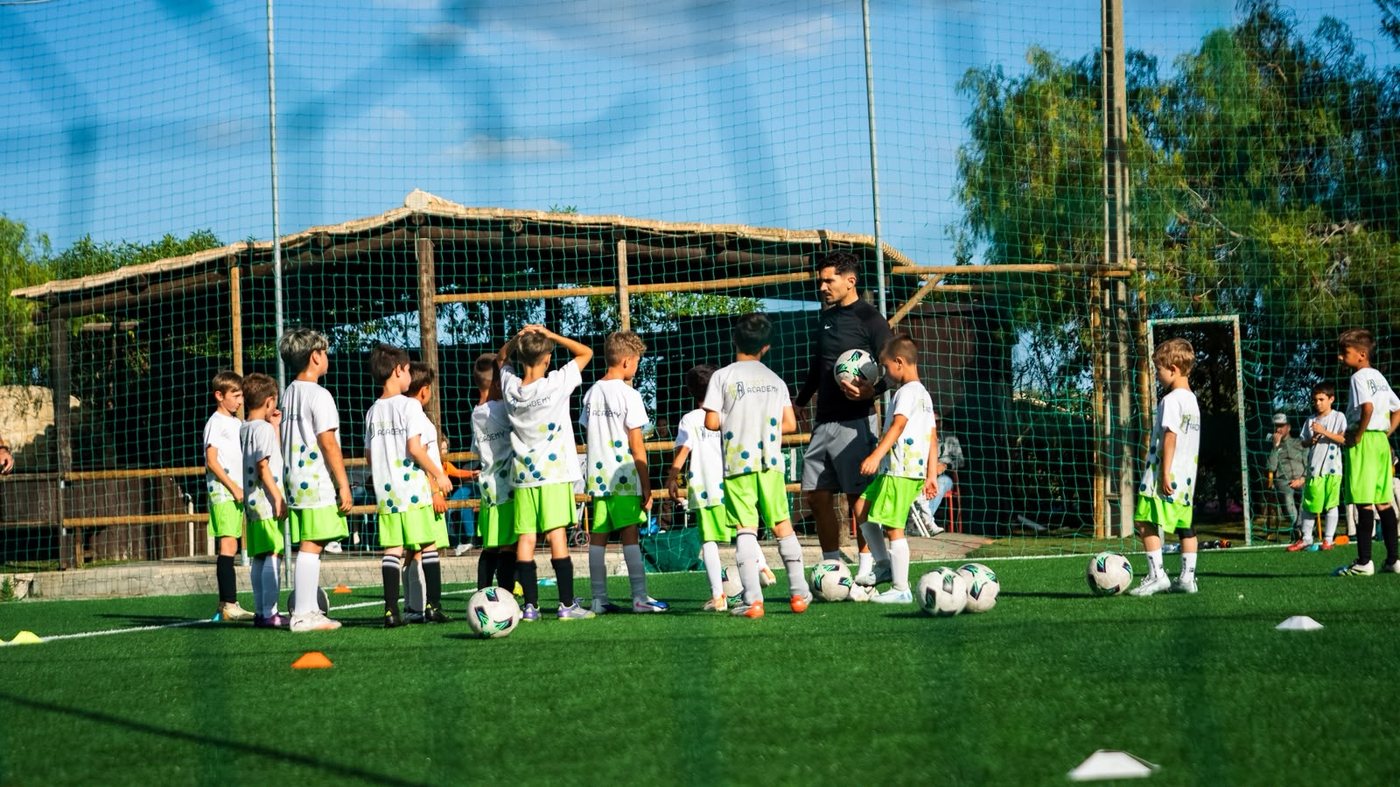 Grupo de atletas da FootAcademy a ouvir o treinador antes do treino